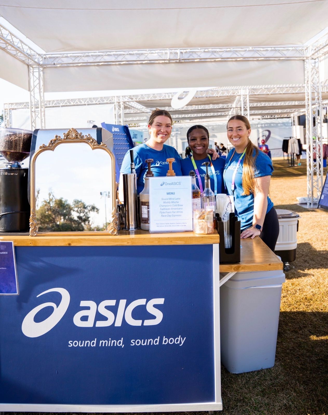 Three baristas behind the ASICS-branded coffee cart under the event tent
