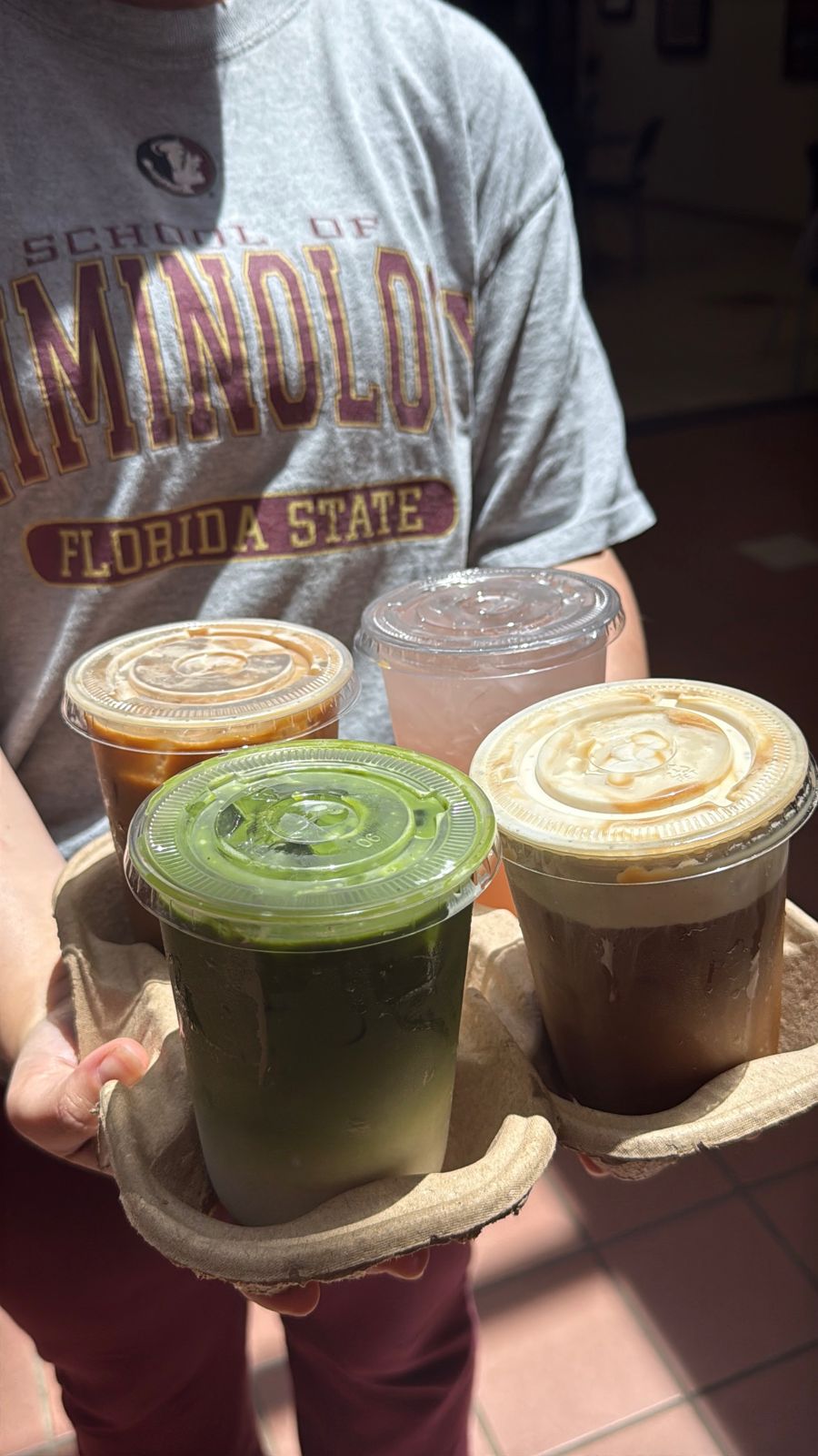 A carrier of four drinks: matcha, iced latte, cold brew and a pink one