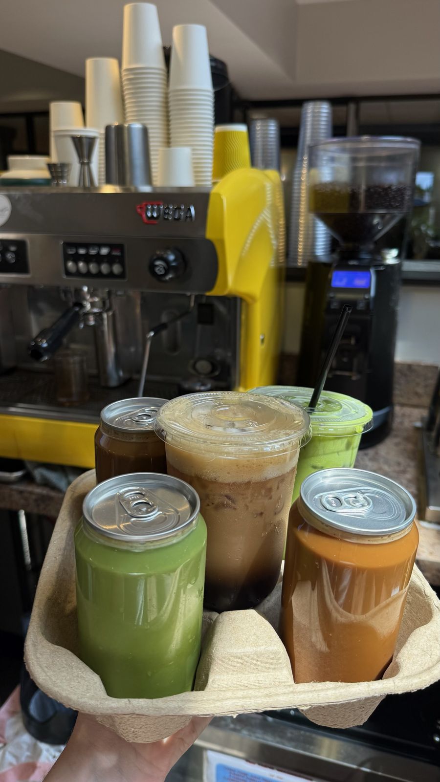 A carrier of four iced drinks held up in front of the espresso machine